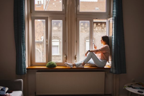 A woman sits comfortably on a windowsill, sipping a drink and looking out at the view from her Budapest apartment in the afternoon sunshine.